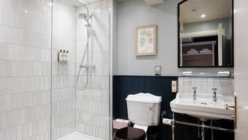 A bathroom with a glass-enclosed shower, a white toilet, a sink with a mirror above it, and a framed artwork on the wall.