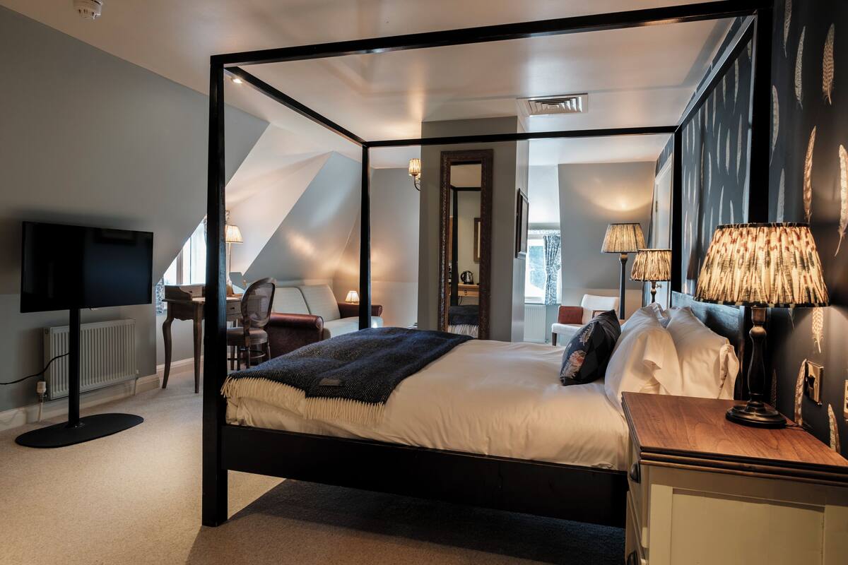 Quarto moderno com cama de dossel, escrivaninha com cadeira, televisão e luminárias.