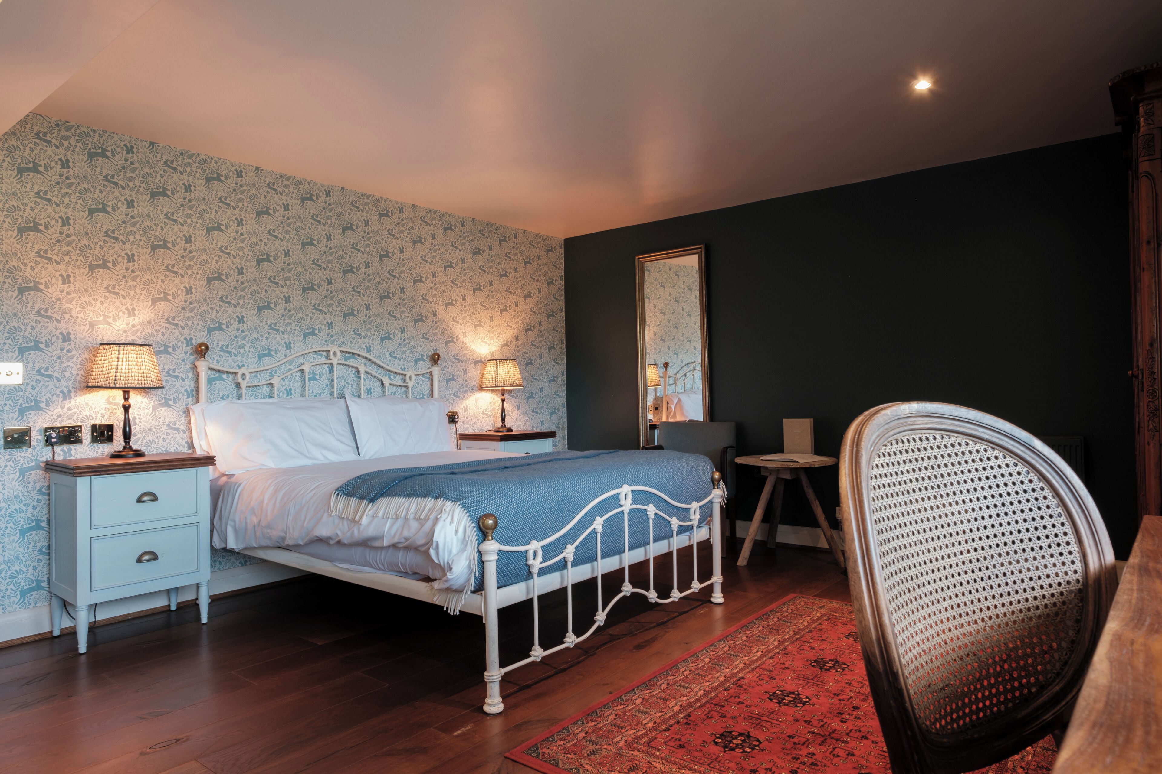 Ein Schlafzimmer mit Bett, Nachttischen, einem Sessel und einem Spiegel.