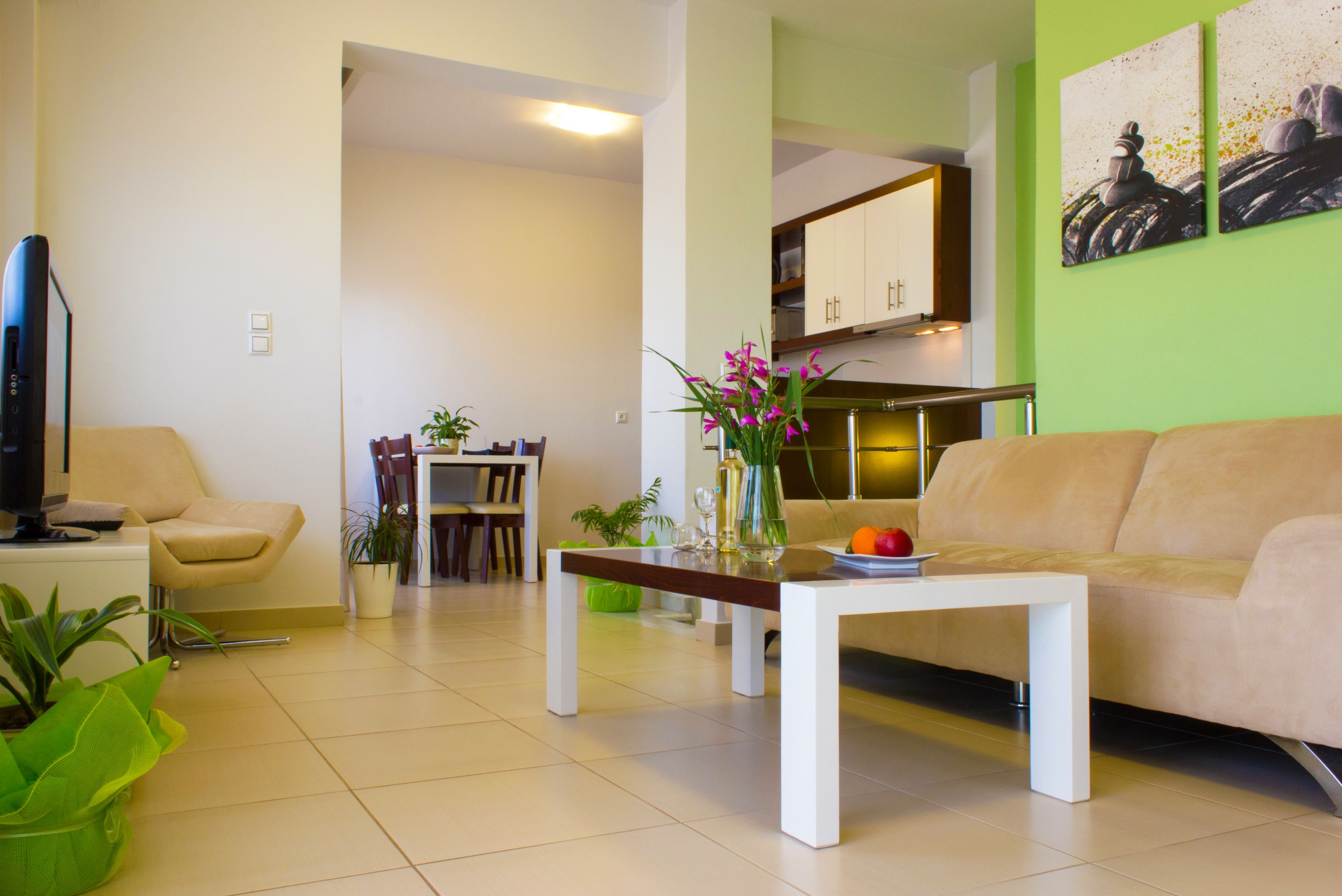 Una sala de estar moderna con un sofá color beige, una mesa de centro y un comedor con mesa y sillas. Hay plantas en macetas y obras de arte en las paredes.