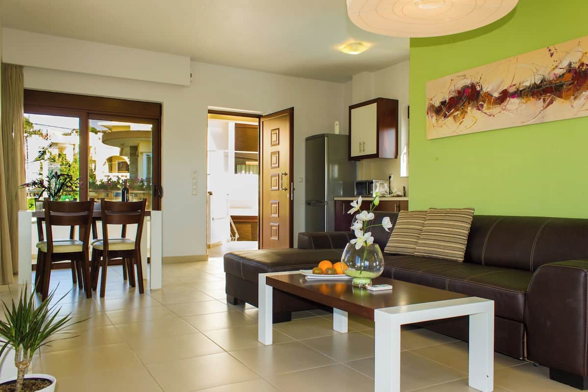 A modern living room with a sofa, a dining table, chairs, and a kitchen area in the background.