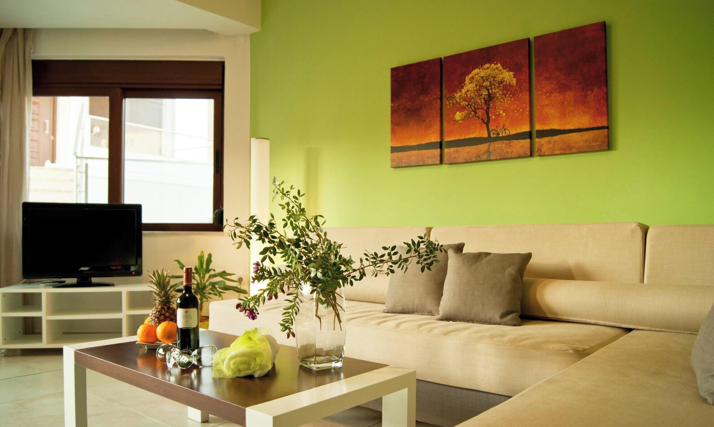 Un salon comprenant un canapé, une table basse agrémentée d’objets décoratifs, un téléviseur et un mur vert orné d’œuvres d’art.