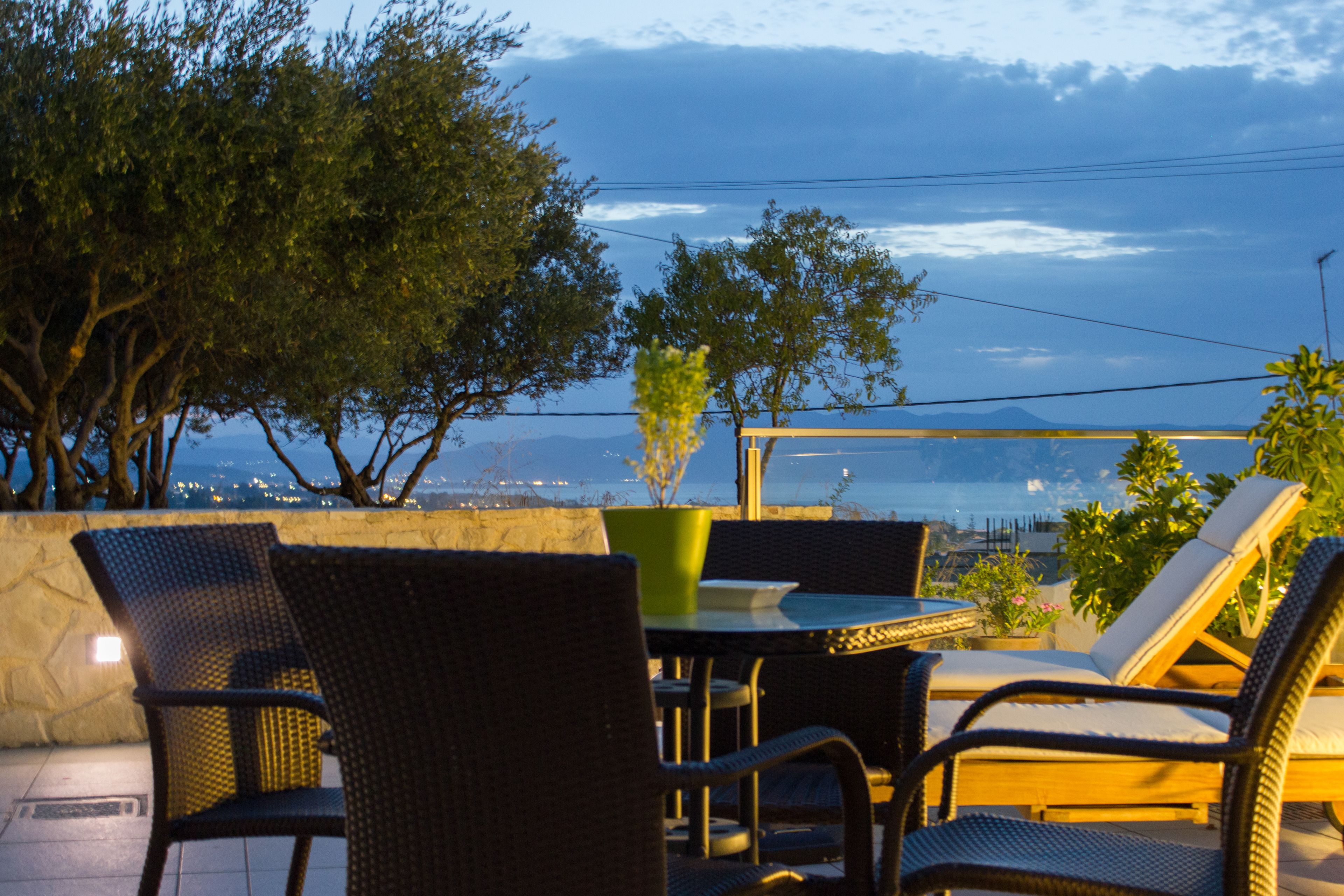Ein Außenbereich mit Korbmöbeln, Stühlen und einem Tisch, mit Blick auf eine schöne Landschaft mit Bäumen und weiter Ferne.