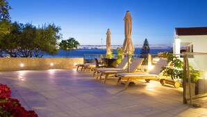 A terrace with lounge chairs and umbrellas, a stone wall, and a view of the sea.