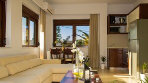 A modern living room with a sofa, a coffee table with decorative items, a dining area with chairs, and a kitchen with appliances.