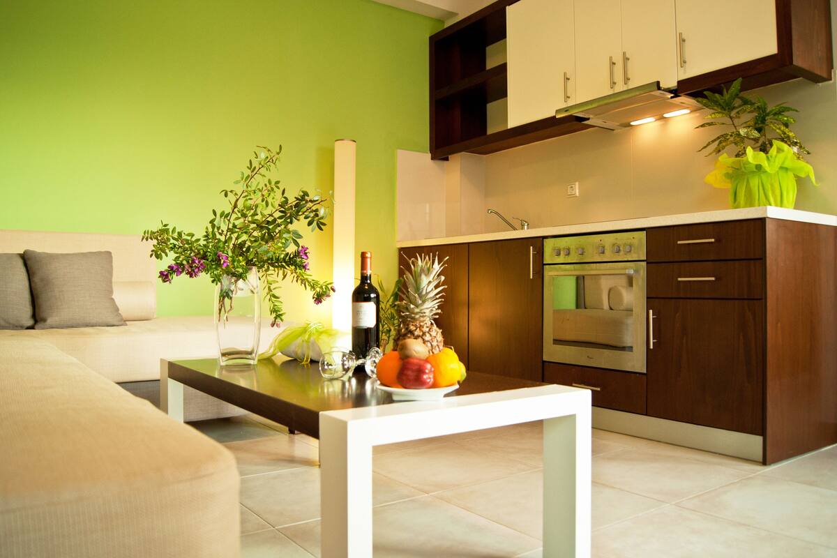 Una cocina moderna con armarios de madera, horno integrado y un comedor con mesa blanca y sofá.