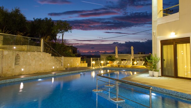 A swimming pool with steps leading into it, surrounded by lounge chairs and a stone wall.