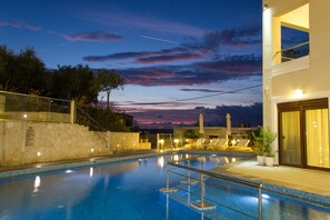 A swimming pool with steps leading into it, surrounded by lounge chairs and a stone wall. - Esthisis Suites Chania (Platanias)