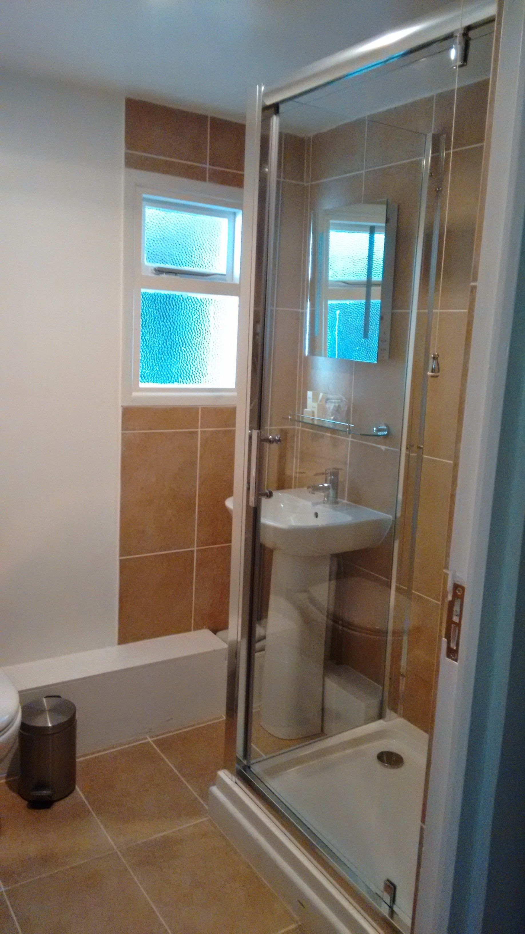 A bathroom with a glass-enclosed shower, a sink, and a window.
