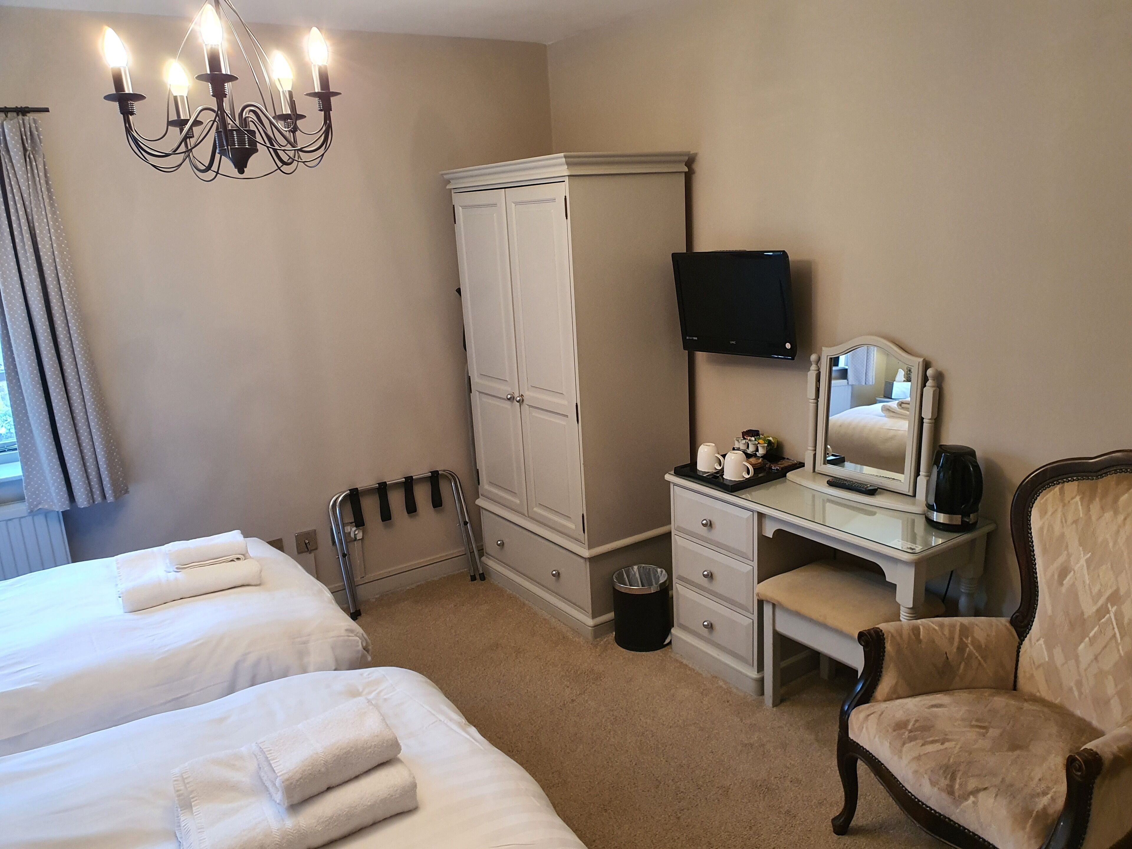 Une chambre d’hôtel avec deux lits, une armoire, un bureau avec un miroir, une chaise et un téléviseur.