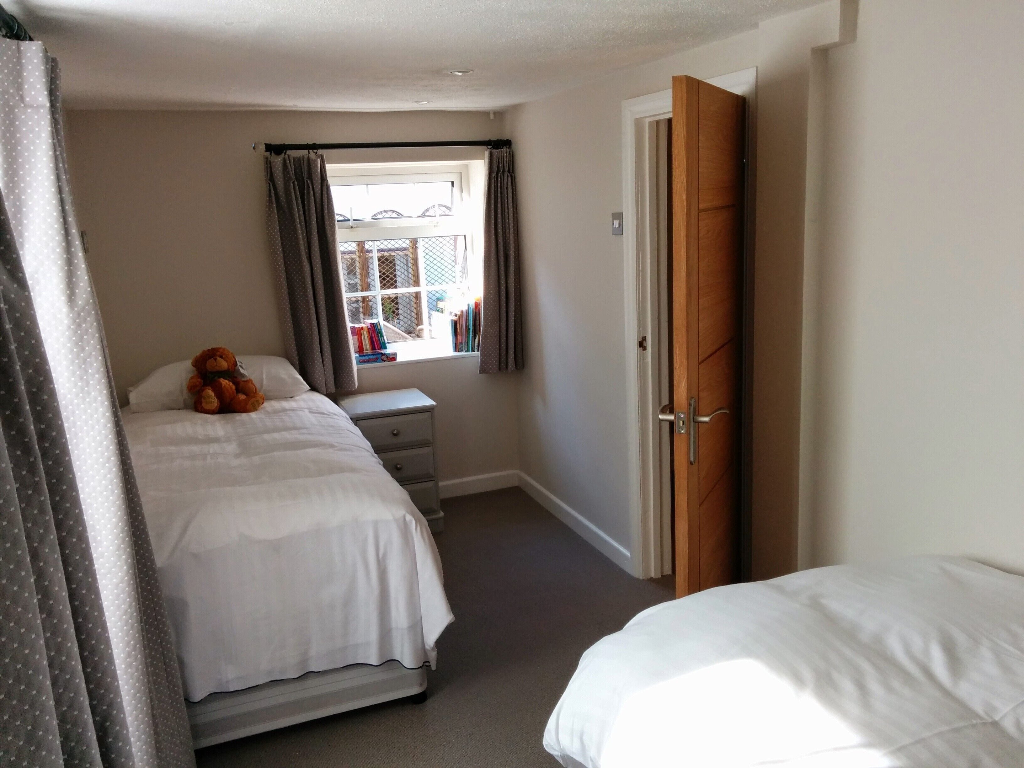 A bedroom with a bed, a bedside table, a window with curtains, and a door.