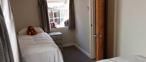A bedroom with a bed, a bedside table, a window with curtains, and a door.
