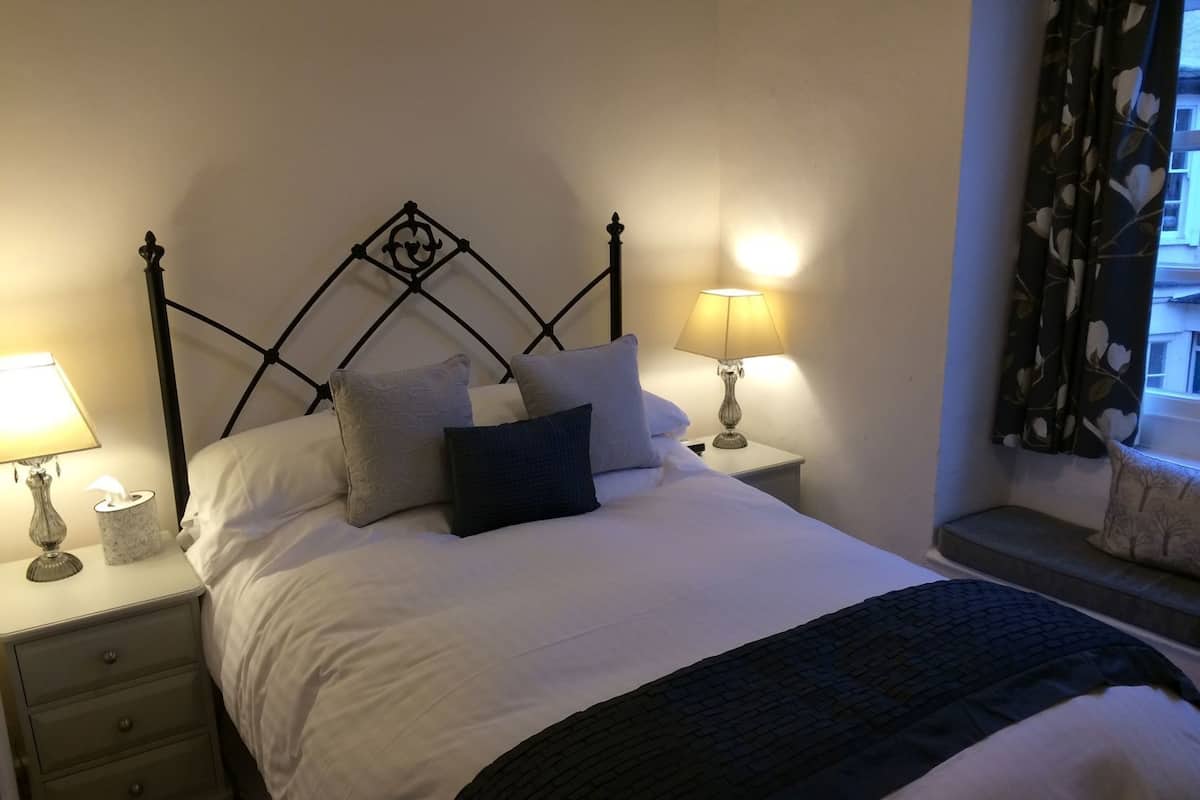 A neatly made bed with white bedding and a black throw blanket, flanked by two bedside tables with lamps, one of which has a tissue box.