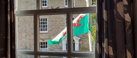 A window with a view of a street, a stone building, and a flag.