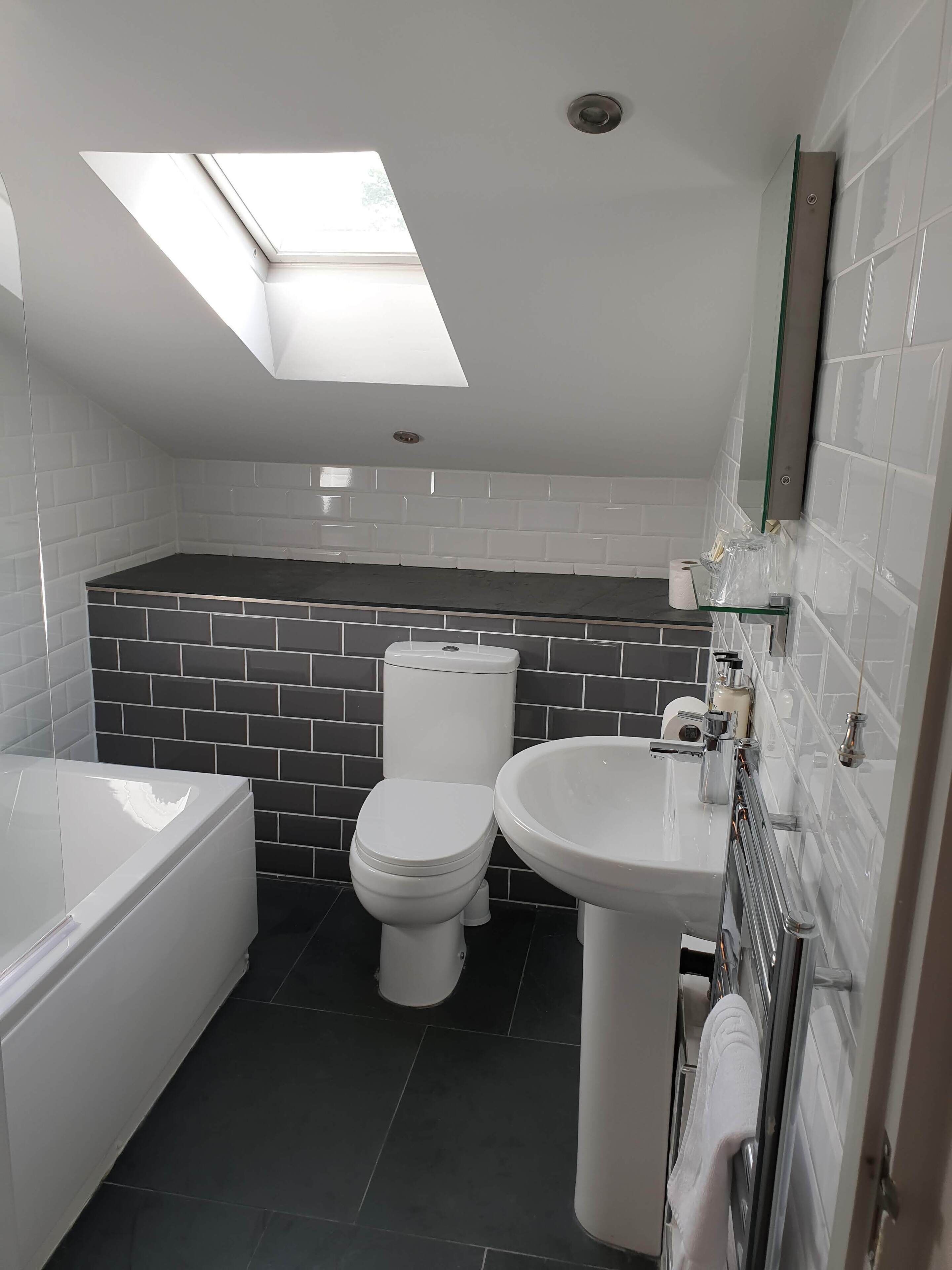 Un baño moderno con tragaluz, bañera, inodoro y lavamanos.
