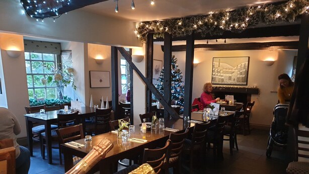 A cozy restaurant with wooden tables and chairs, a Christmas tree, and a fireplace.