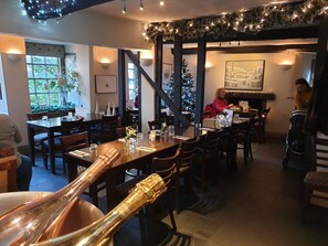 A cozy restaurant with wooden tables and chairs, a Christmas tree, and a fireplace. - Dragon Inn Crickhowell (Crickhowell)