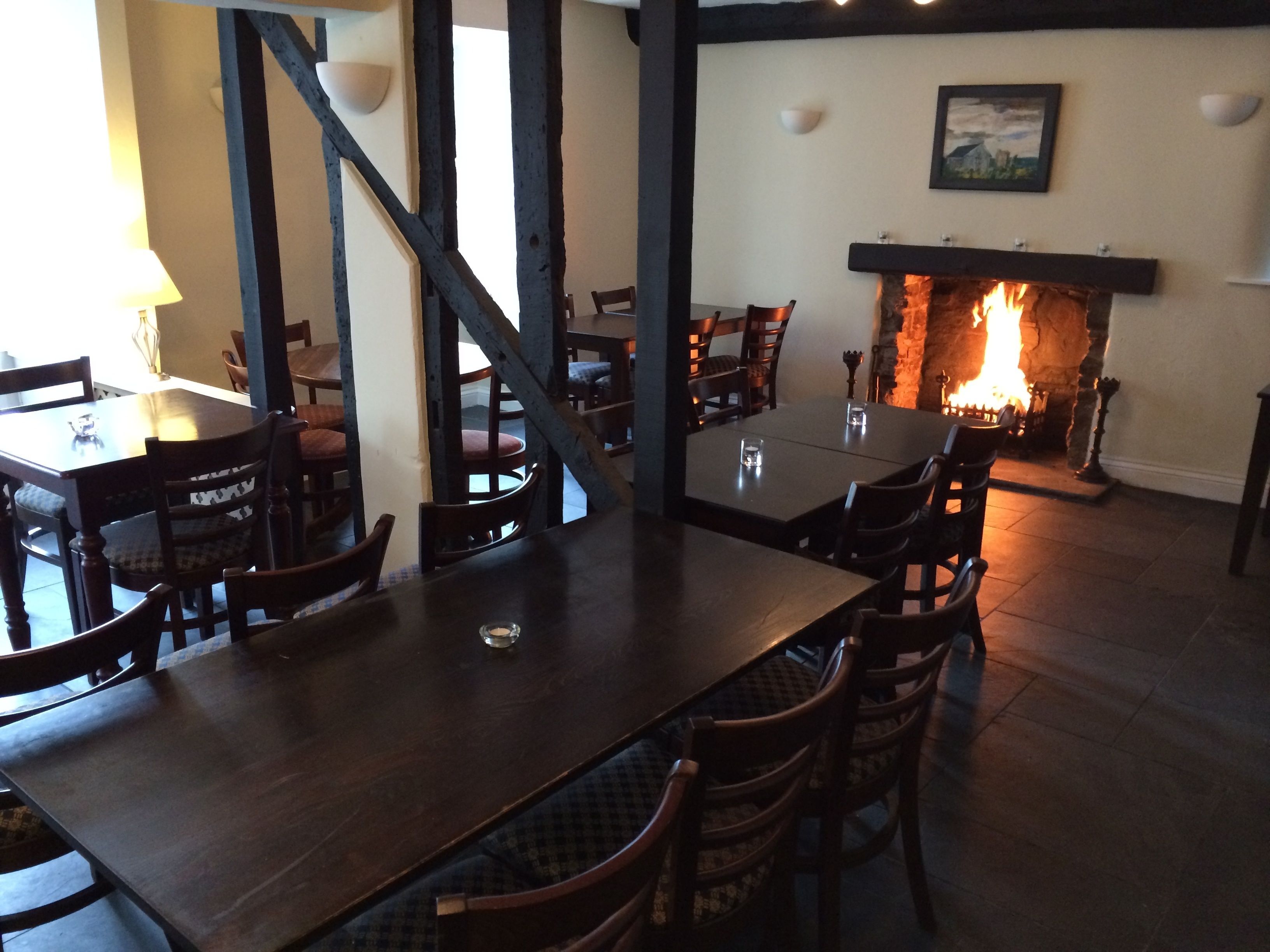 Un interior de restaurante con mesas y sillas de madera, una chimenea y una pared de piedra.