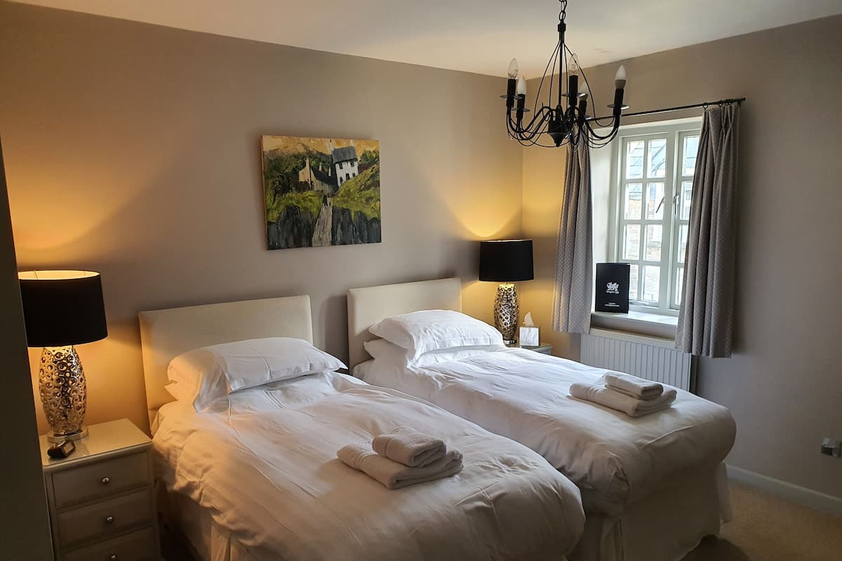 A hotel room with two beds, a chandelier, a painting, and a window with curtains.
