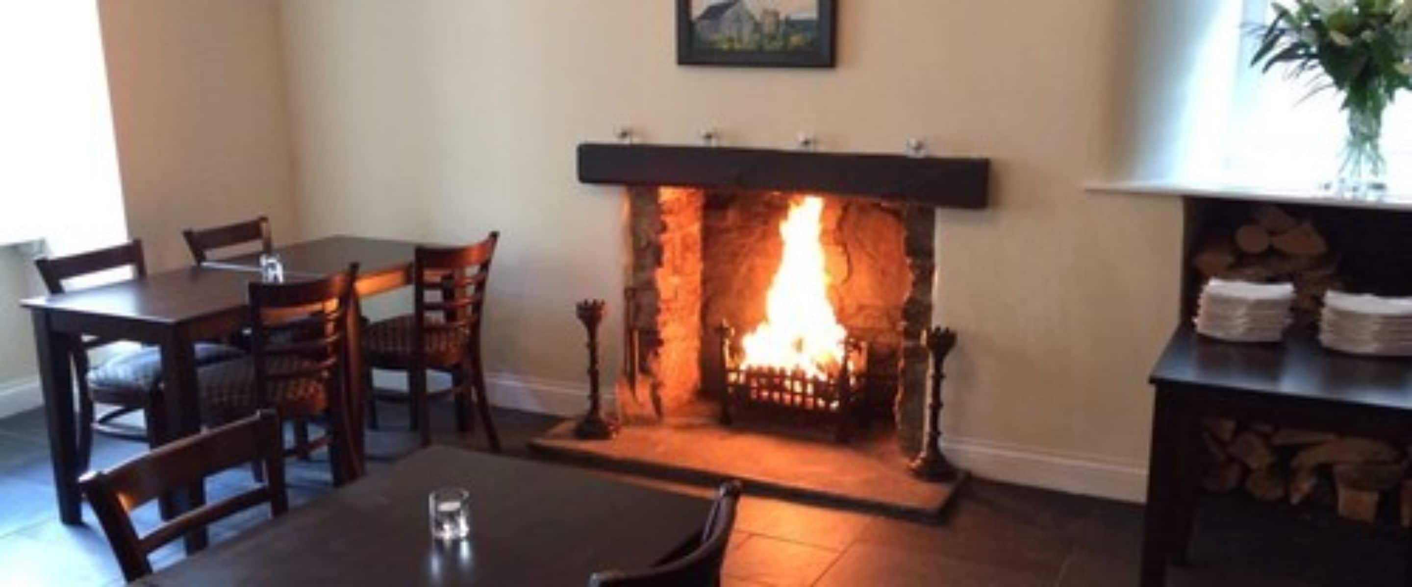 A room with a fireplace, a dining table with chairs, and a small side table with a glass.