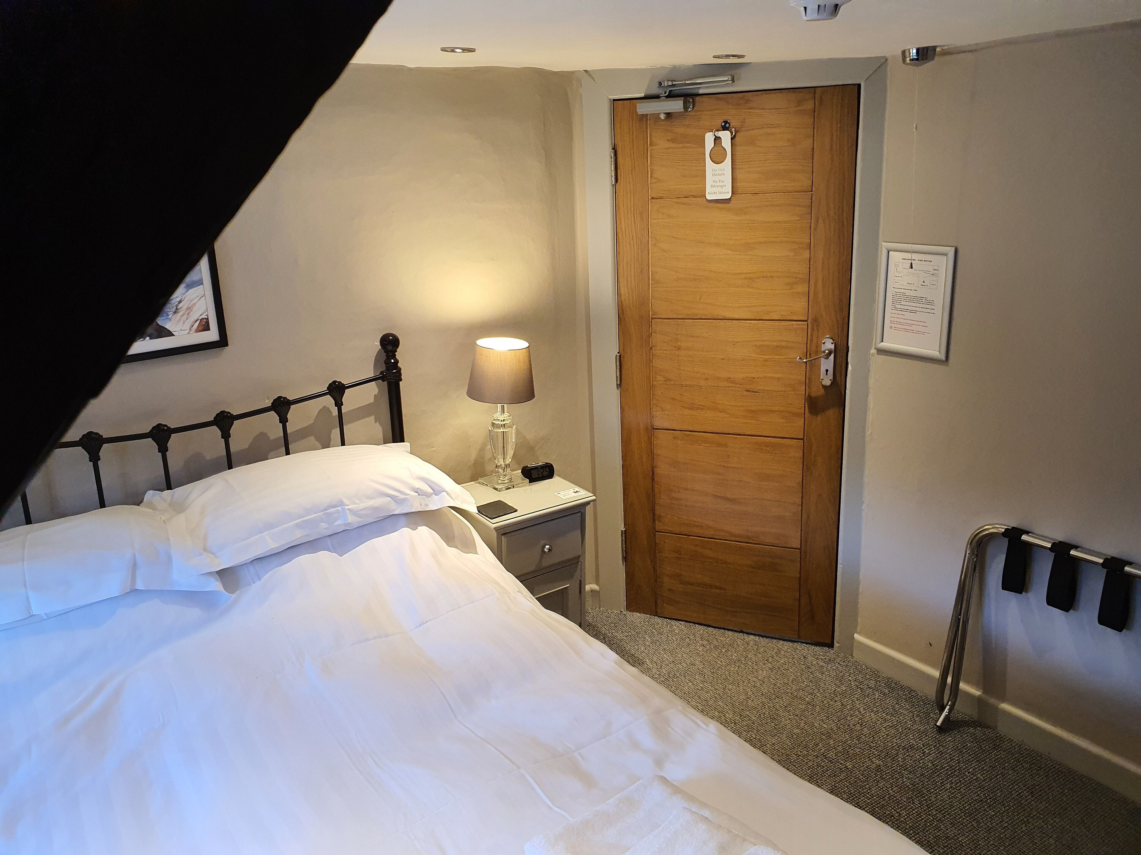 A hotel room with a bed, a nightstand, a lamp, a wooden door, and a wheelchair ramp.