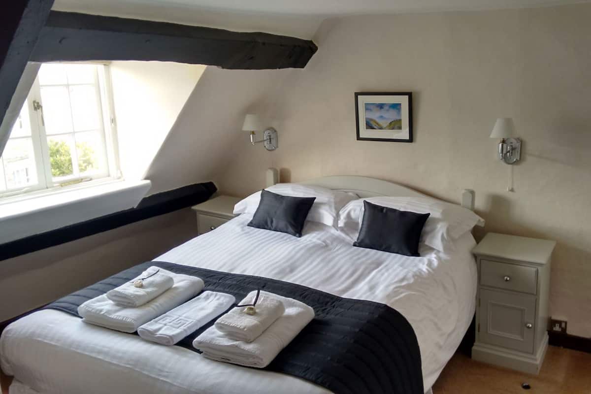 A bedroom with a large bed, two bedside tables, a window, and a painting on the wall.