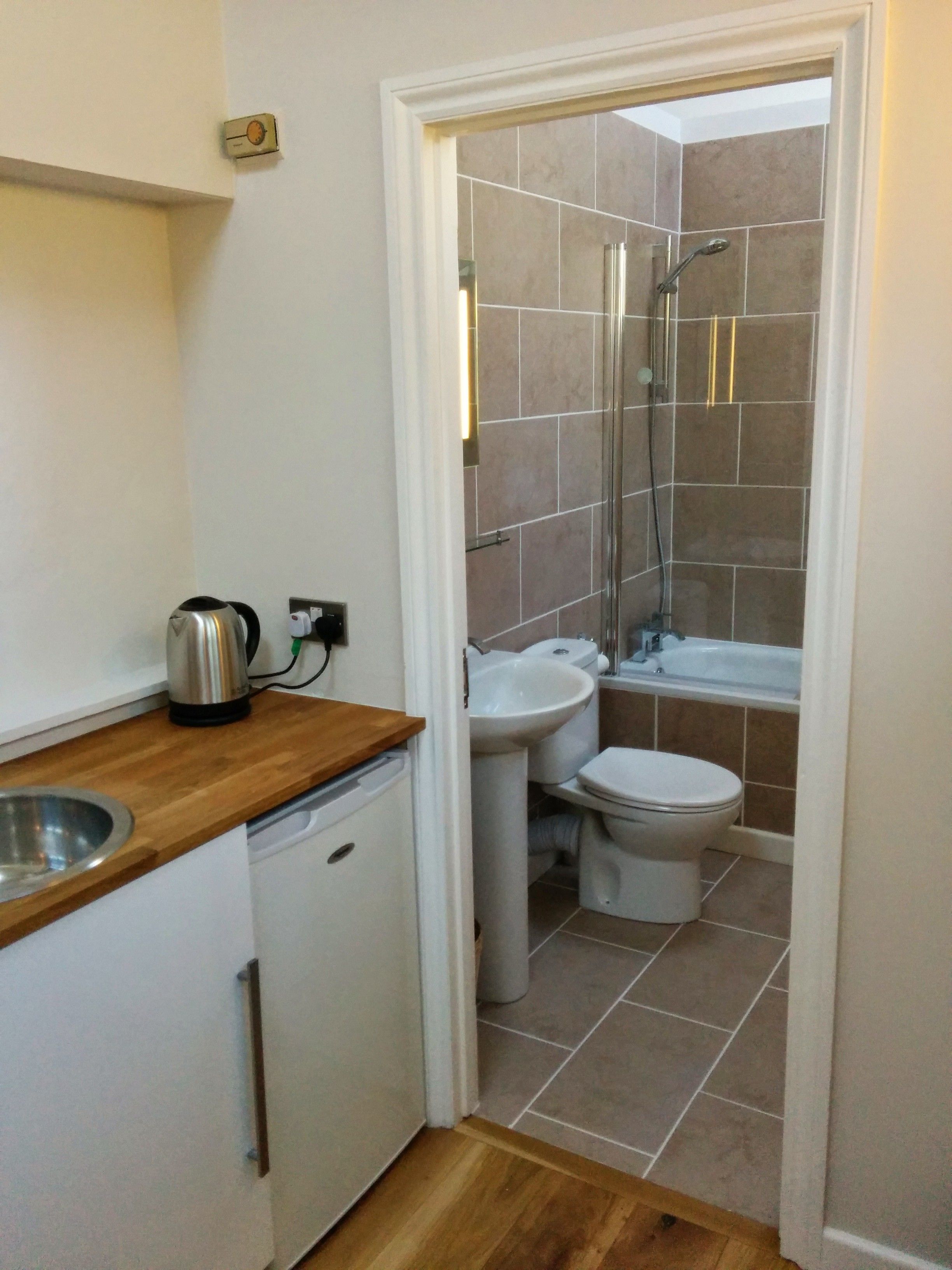 A compact bathroom with a shower, toilet, sink, and a small kitchen area with a kettle.