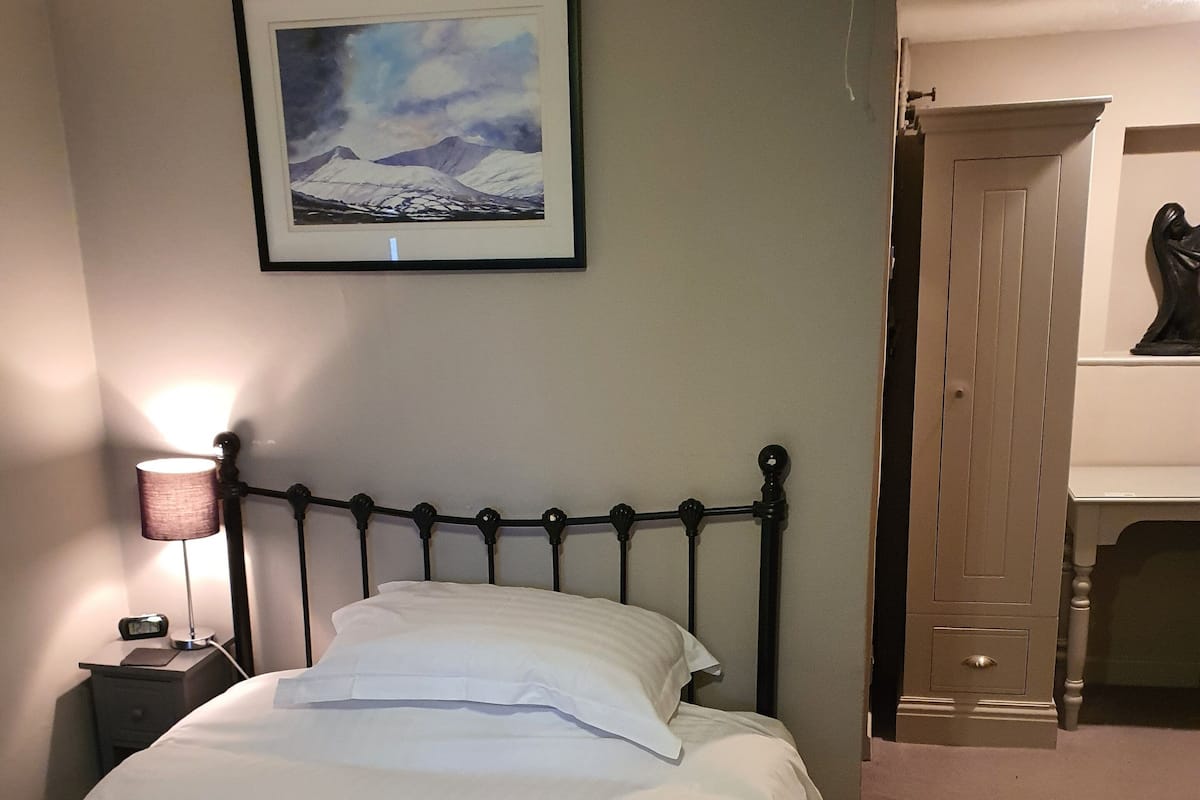 A neatly made bed with white linens and pillows, a bedside lamp, and a framed picture on the wall.