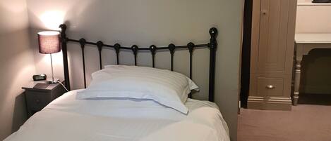 Una cama bien tendida con sábanas y almohadas blancas, una lámpara de noche y un cuadro en la pared.