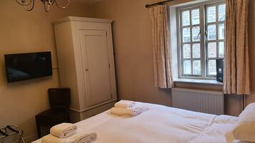 Quarto de hotel com cama, guarda-roupa, televisão e janela com cortinas.