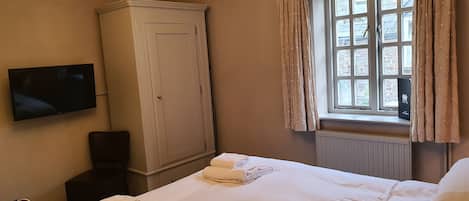 Una habitación de hotel con cama, armario, televisor y ventana con cortinas.