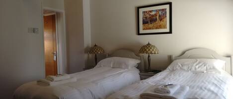 Habitación de hotel con dos camas, cada una con ropa blanca y toallas, un cuadro en la pared y dos lámparas en las mesitas de noche.