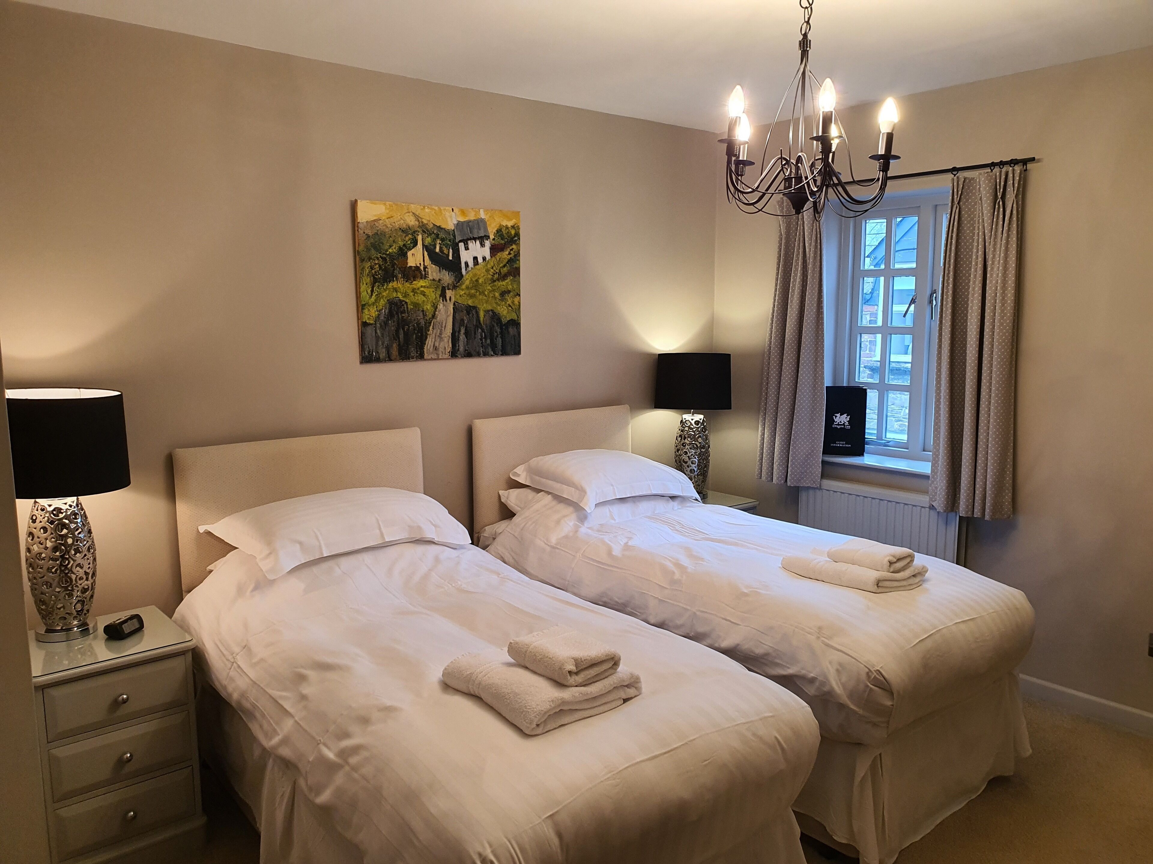 Habitación doble con dos camas, un candelabro, un cuadro, una lámpara y una ventana con cortinas.