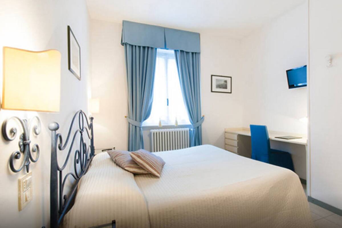 A bedroom with a bed, a desk, a chair, a radiator, and a window with curtains.