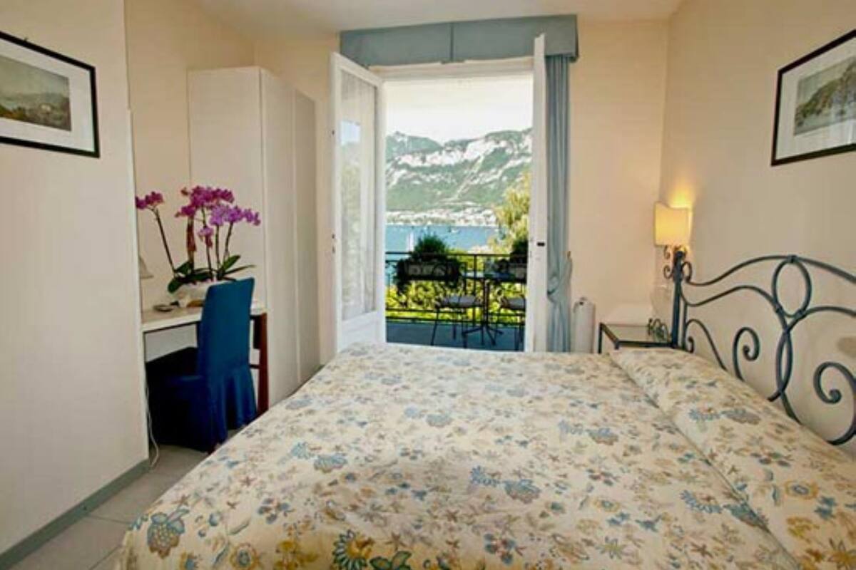A bedroom with a bed, a desk, a chair, and a balcony with a view of mountains.