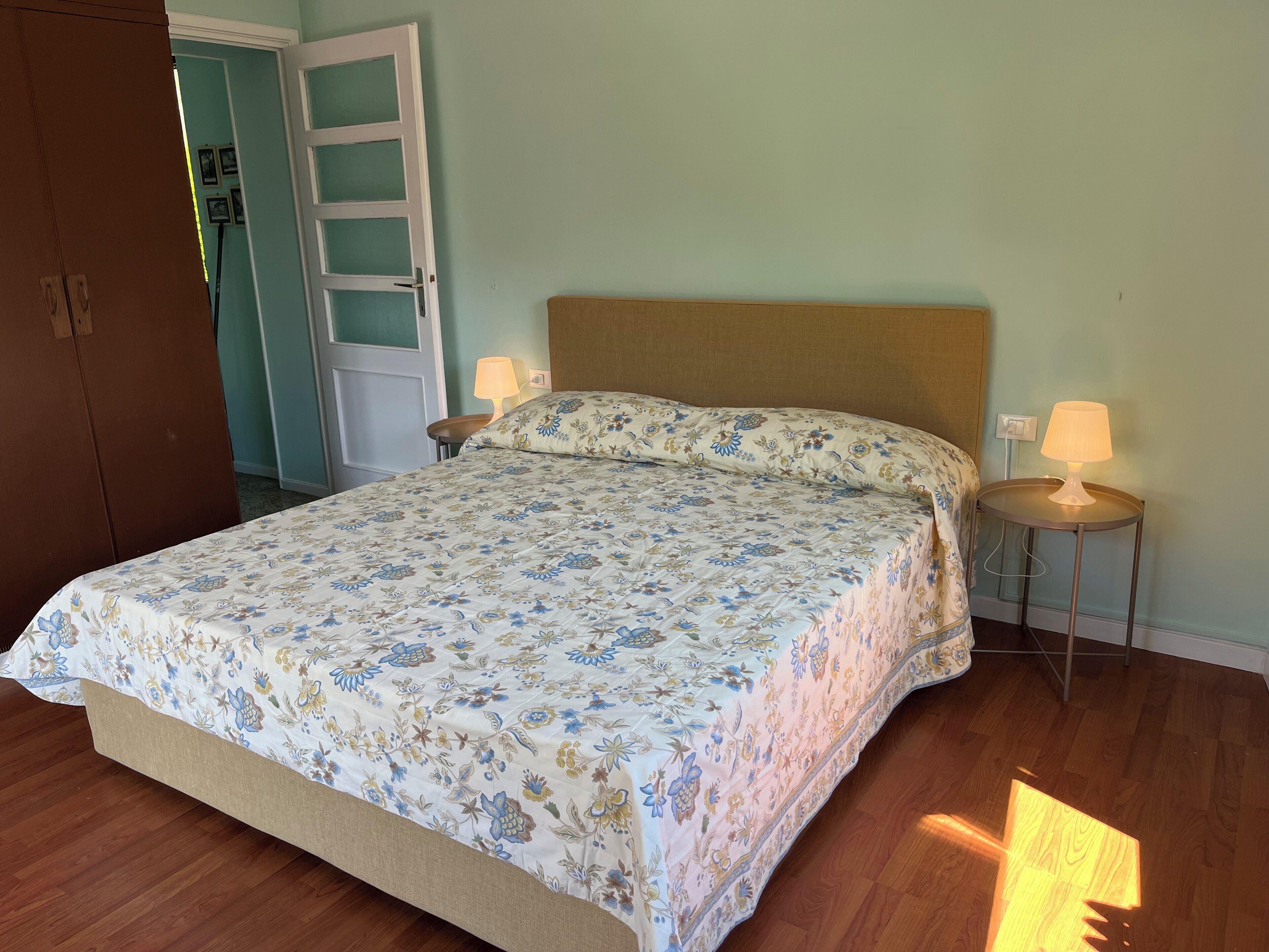 Ein Schlafzimmer mit einem Bett, zwei Nachttischlampen, einem Holzschrank und einer Tür zu einem anderen Raum.