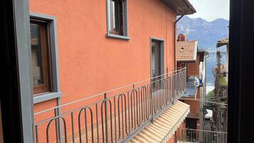 Ein Balkon mit Metallgeländern, einer roten Stuckwand und Blick auf Berge und Wasser.