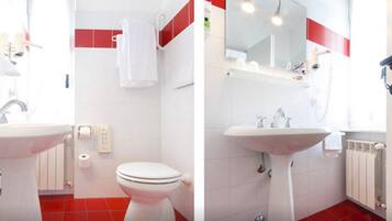 Un baño con lavamanos blanco, inodoro y suelo de baldosas rojas.