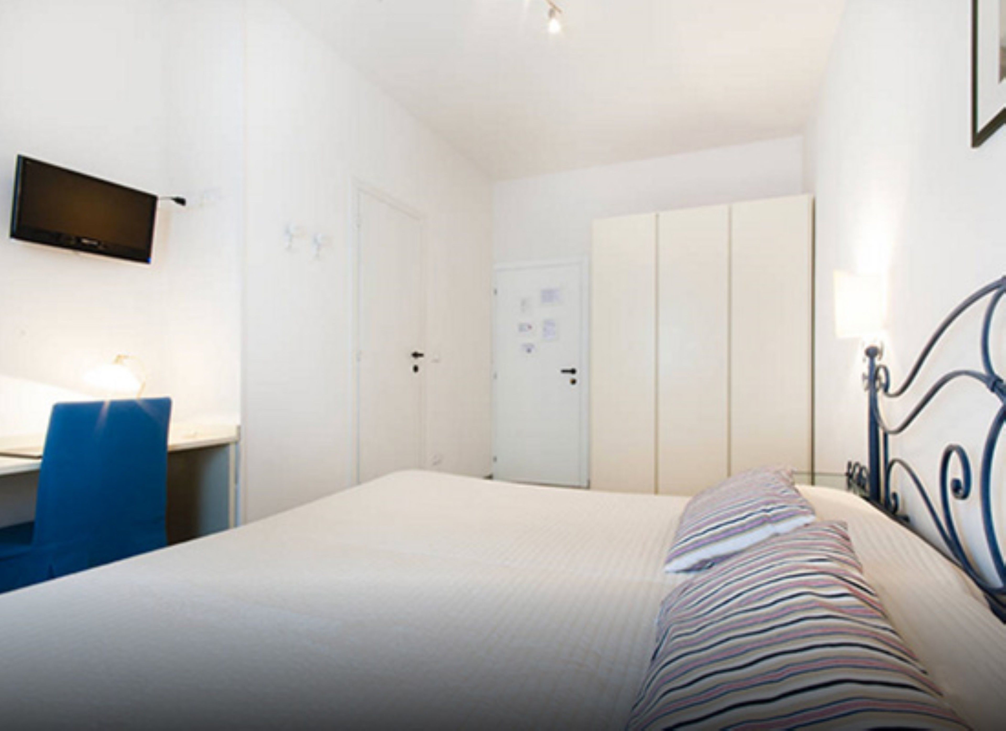 Une chambre à coucher avec un lit, un bureau et une chaise. On y trouve également une armoire et un téléviseur fixé au mur.