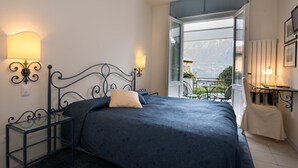 Een slaapkamer met een bed, bedlampen, een klein tafeltje en uitzicht op een balkon met buitenmeubilair.