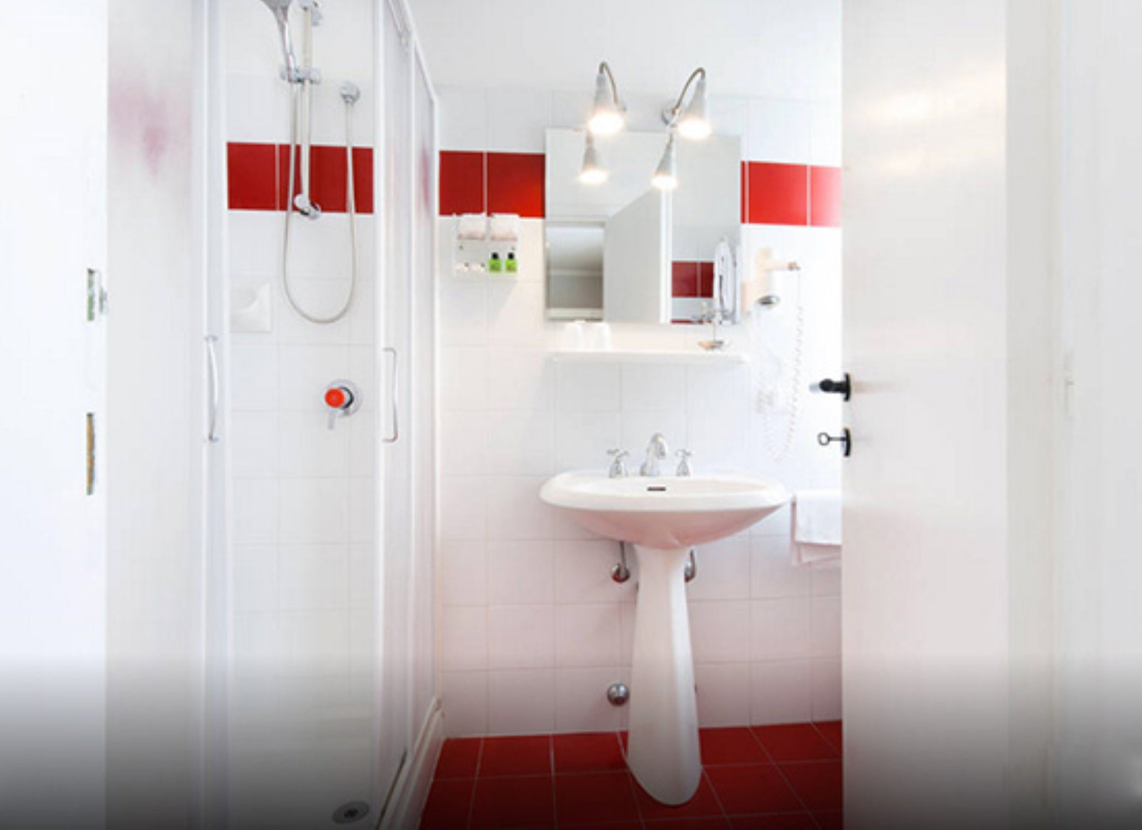 Un baño moderno con ducha envuelta en vidrio, lavamanos blanco y suelo de baldosas rojas.