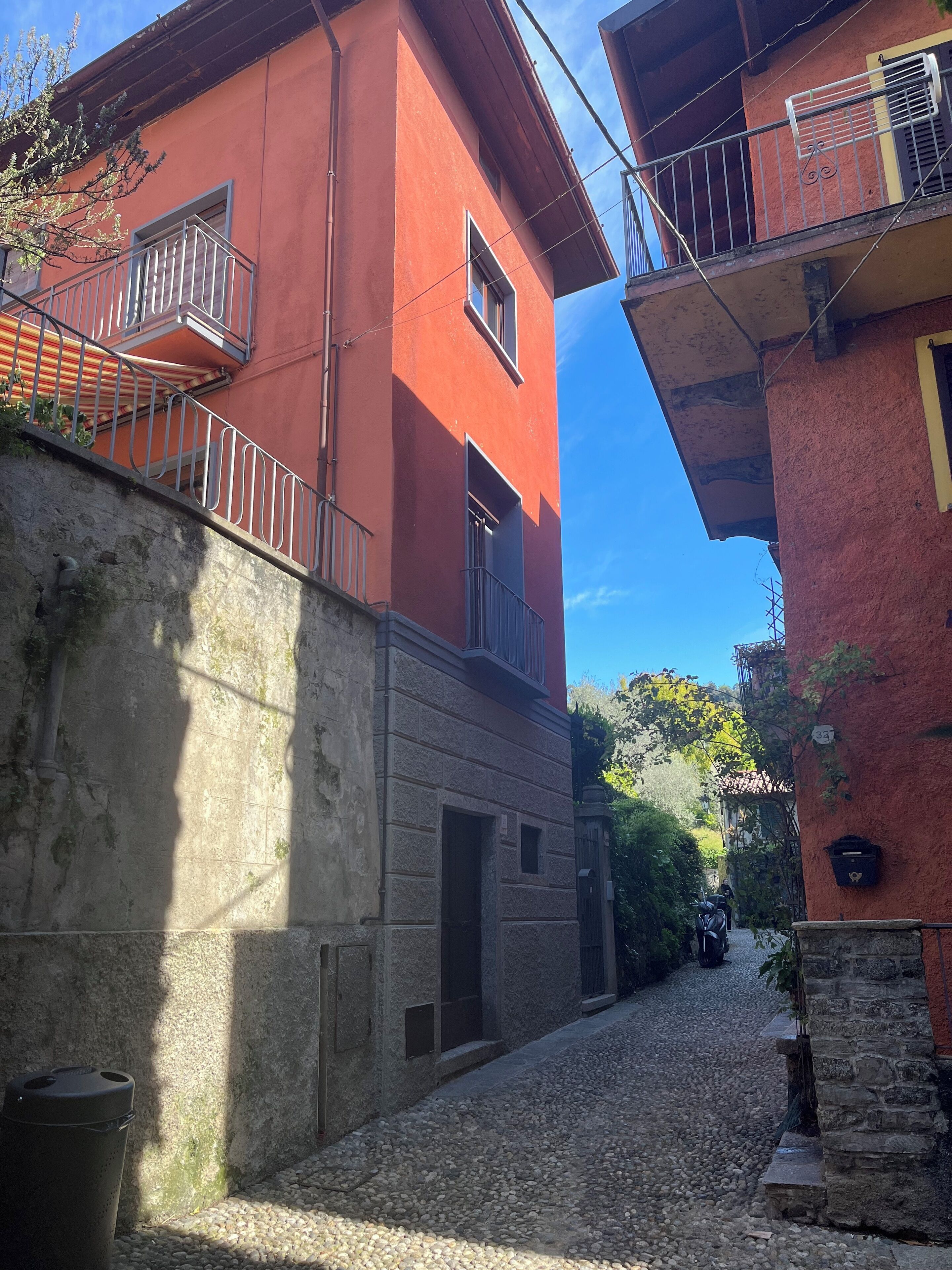 Un estrecho callejón empedrado flanqueado por edificios con balcones y una pared de piedra.