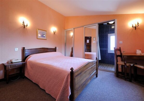A bedroom with a bed, bedside table, lamp, and a desk with a chair. - Les Géraniums (Le Barroux)