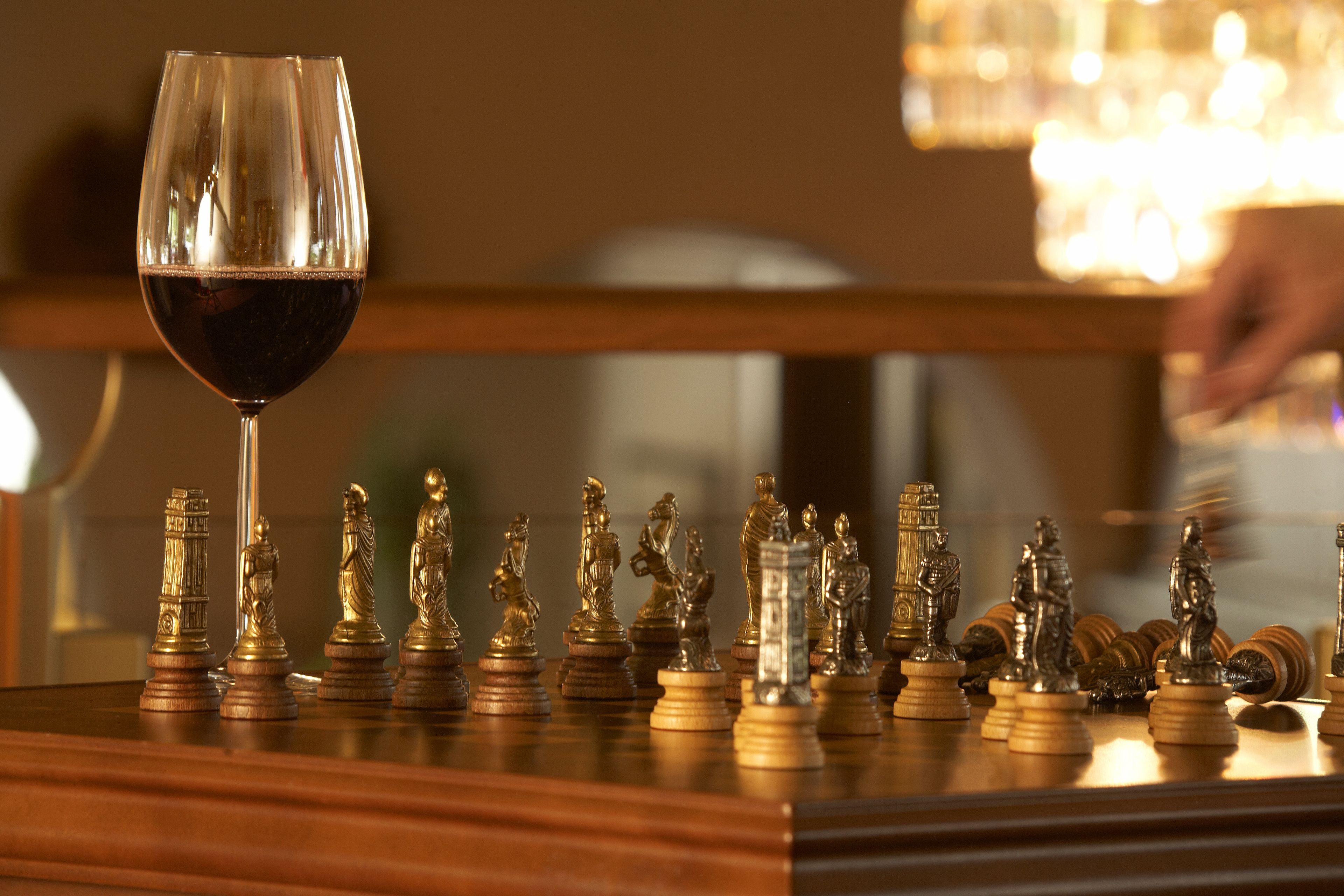A chessboard with chess pieces and a glass of red wine on a wooden surface.