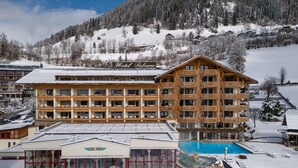 A hotel with multiple floors, a swimming pool, and a ski slope in the background. - Thermenwelt Hotel Pulverer (Bad Kleinkirchheim)