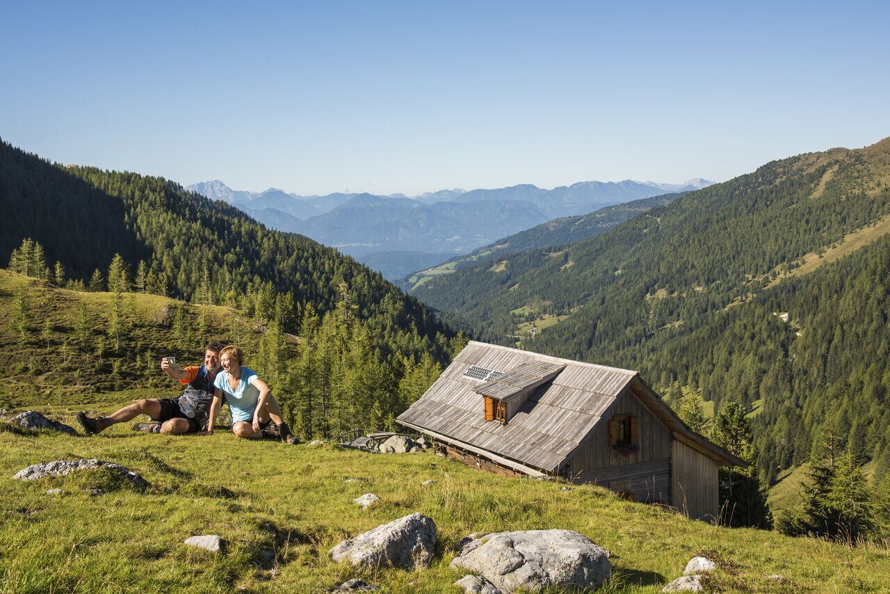 Ein rustikales Holzhaus in einer Bergregion mit freiem Blick auf das Tal und die fernen Berge.