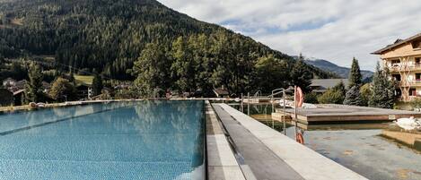 Una piscina con montañas al fondo, terraza de madera y un flotador salvavidas.
