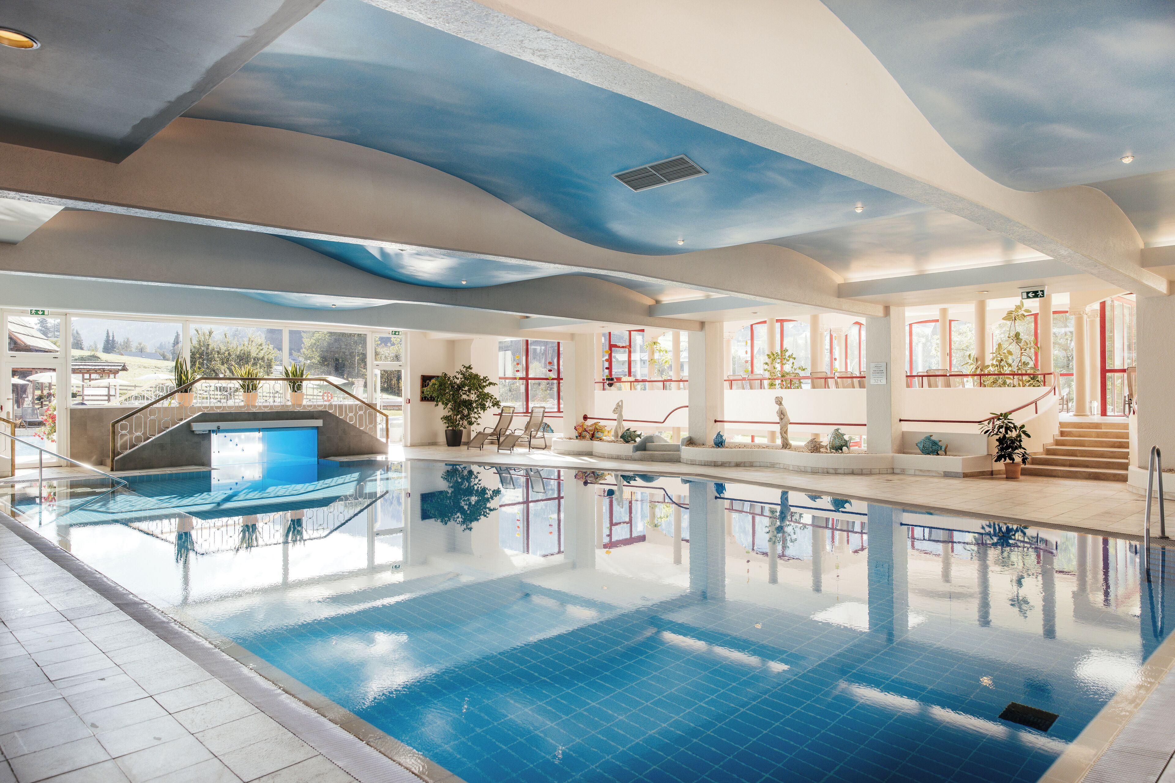 An indoor swimming pool with clear blue water, a tiled floor, and a ceiling with a wave-like design.