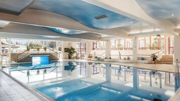 An indoor swimming pool with clear blue water, a tiled floor, and a ceiling with a wave-like design.