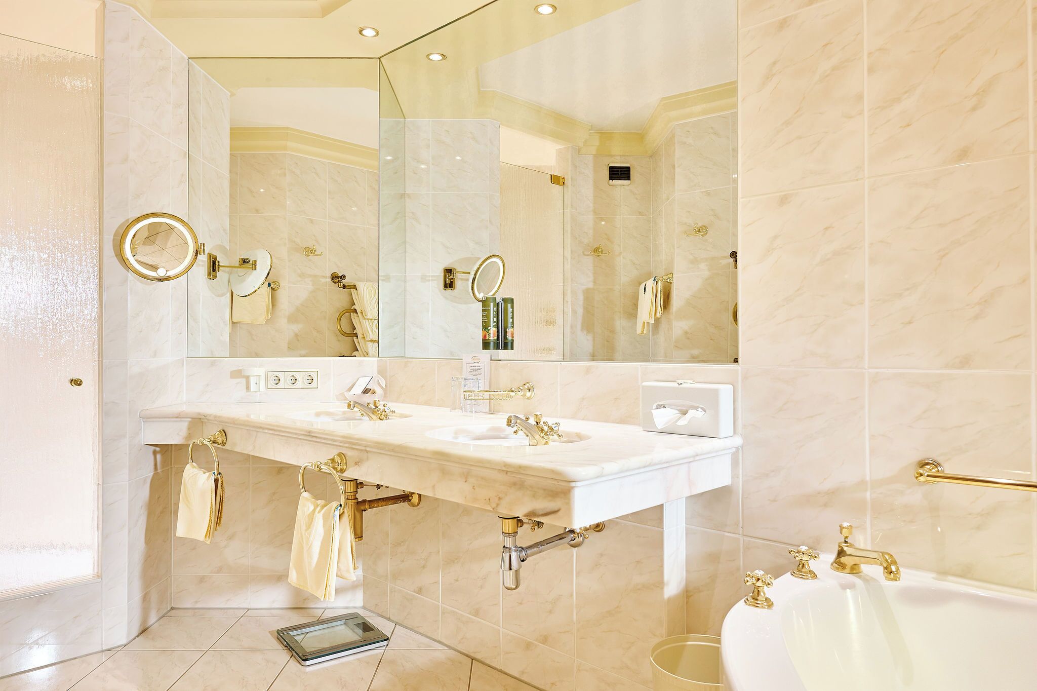 A luxurious bathroom with a large mirror, two sinks, a bathtub, and gold fixtures.